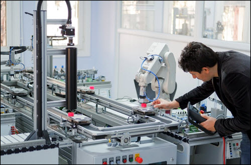 Technician holding a teach panel (tablet) to control a robotic arm