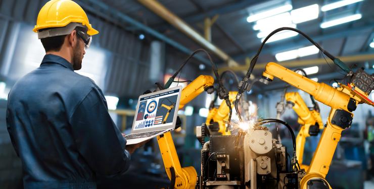 man with programming laptop monitoring robotic arms